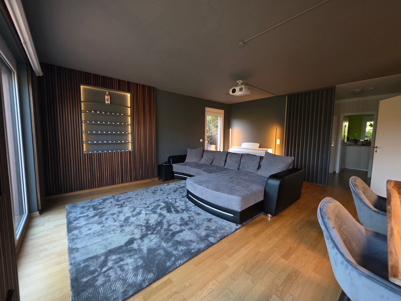 Nachher: Lounge mit Nussbaum-Lamellenwand, beleuchteter Regalnische, Sofa und Beamer